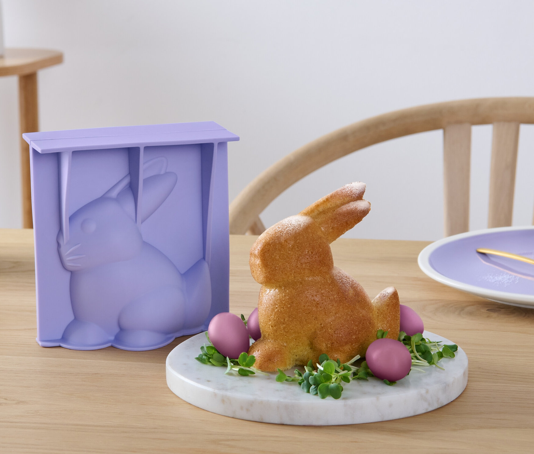 Forma na pečení ve tvaru velikonočního zajíčka stojí vedle upečeného zajíčka na stole.