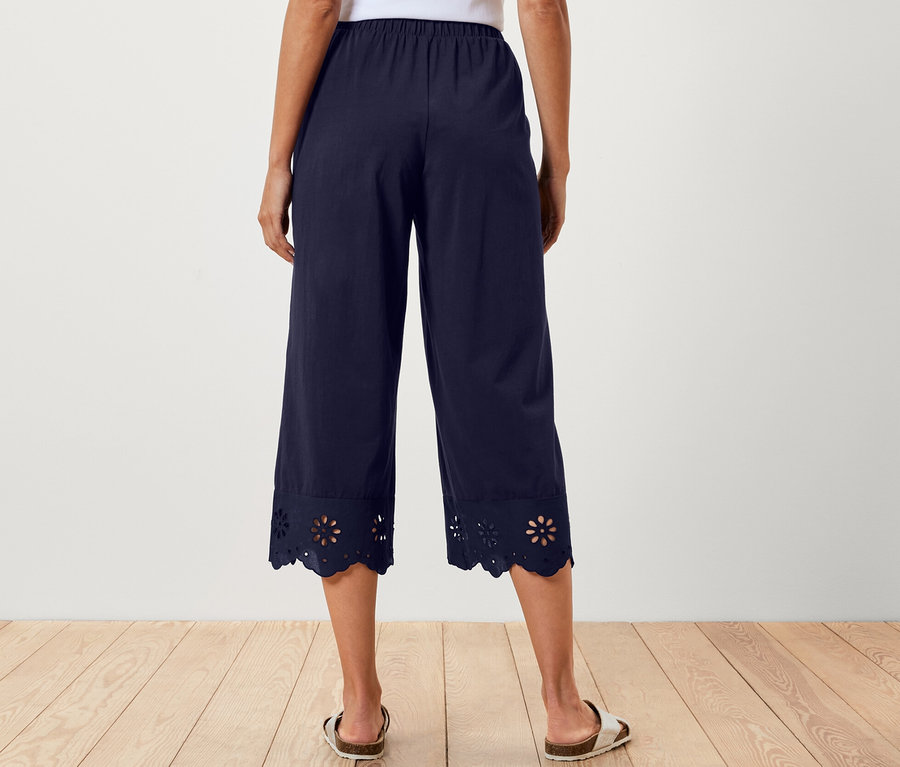 Žena zezadu v bílém topu a tmavě modrých culottes kalhotách s výšivkou na lemu.