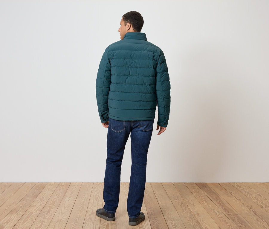 Muž zády k fotoaparátu má na sobě zelenou péřovou bundu, džíny a boty.
