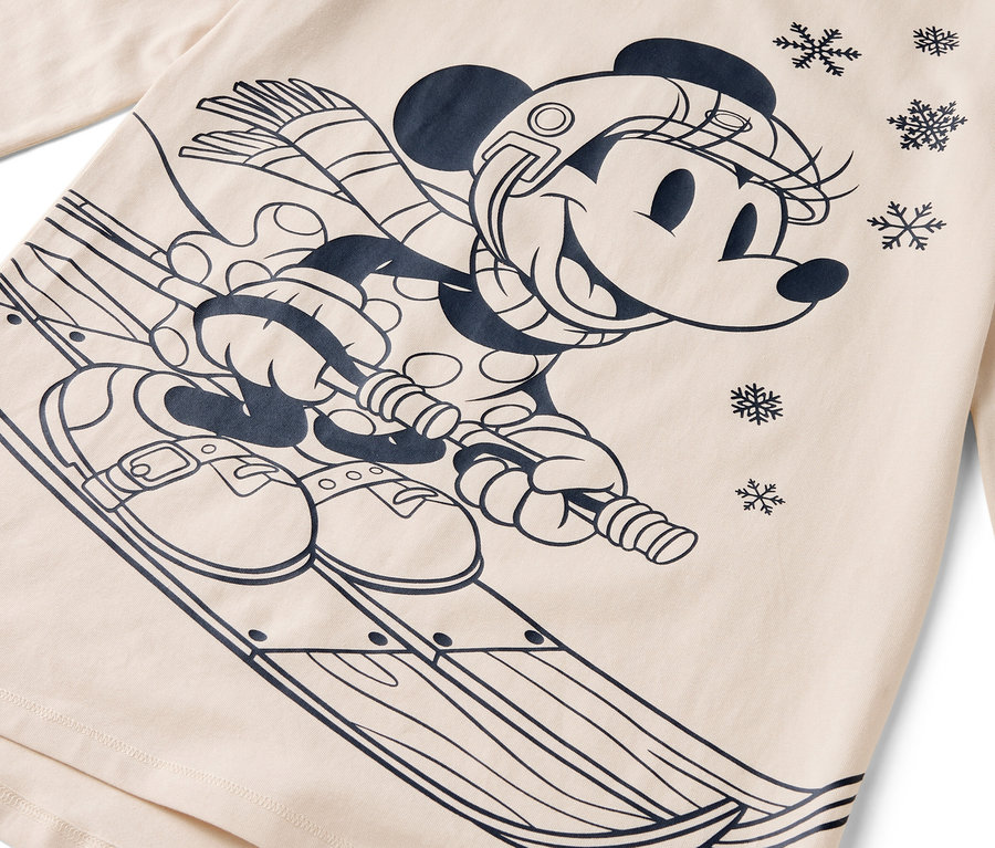 Kreslená postavička myšky Minnie na lyžích s helmou, šálou a rukavicemi na béžovém pozadí.