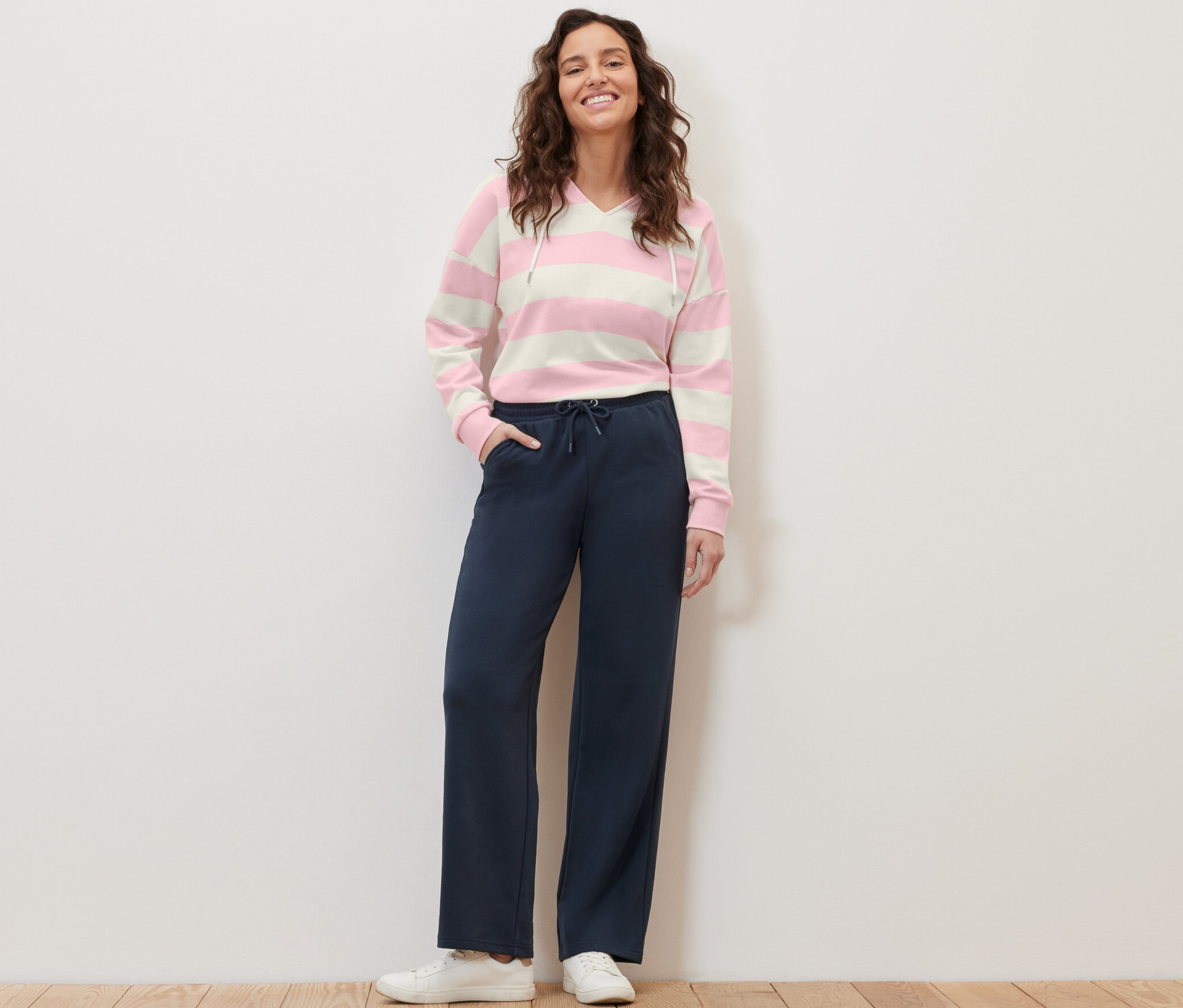 Žena stojí a pózuje v tmavě modrých teplákových kalhotách a pruhované mikině.