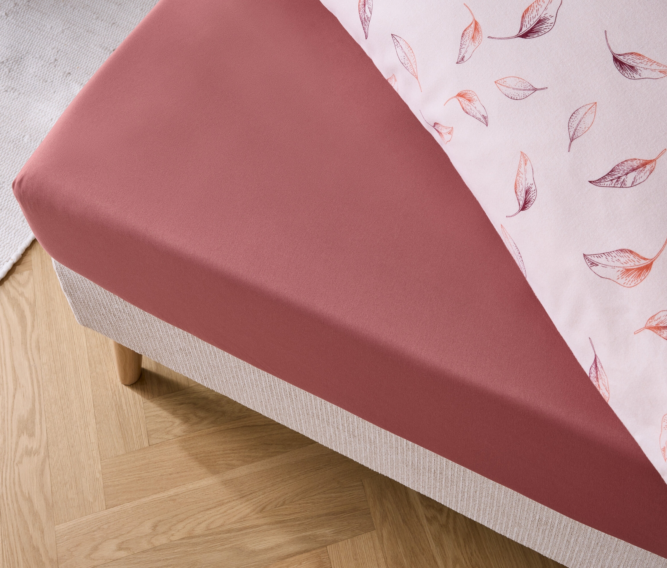 Detail červeného prostěradla a povlaku na polštář s potiskem listů na posteli.
