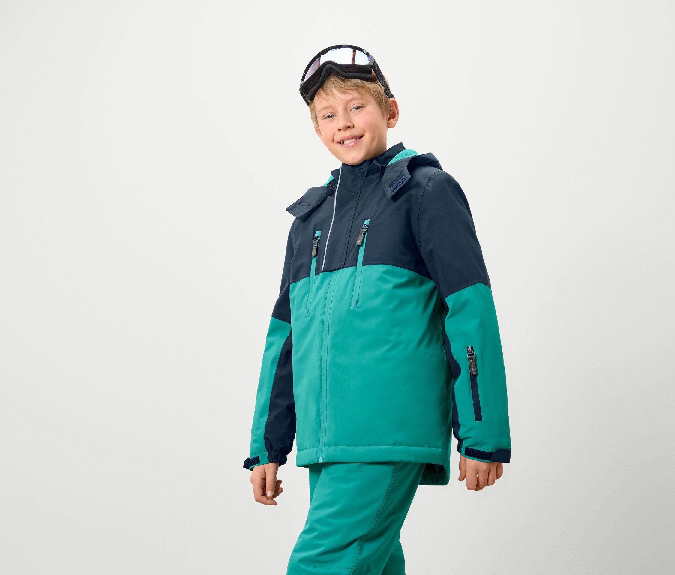 Chlapec v lyžařské bundě a kalhotách, na hlavě má lyžařské brýle.