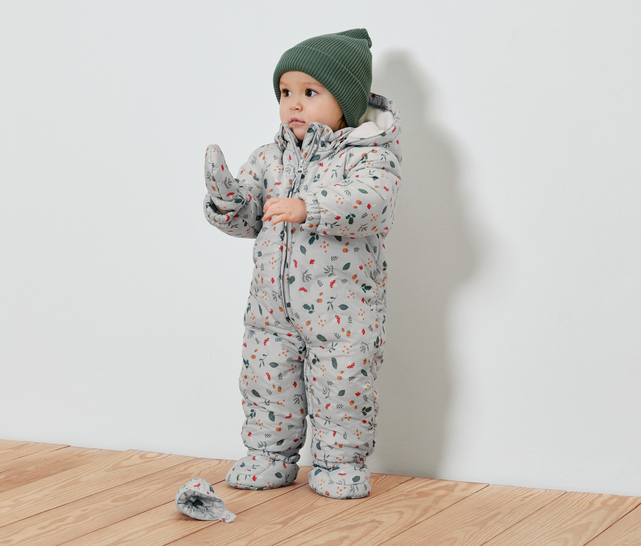 Batole v zimní kombinéze s rostlinným potiskem a zelené čepici.