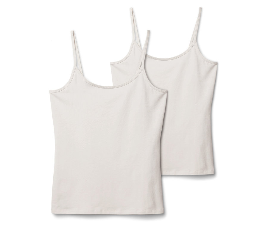 Dvě bílá tílka s tenkými ramínky leží vedle sebe na bílém pozadí.