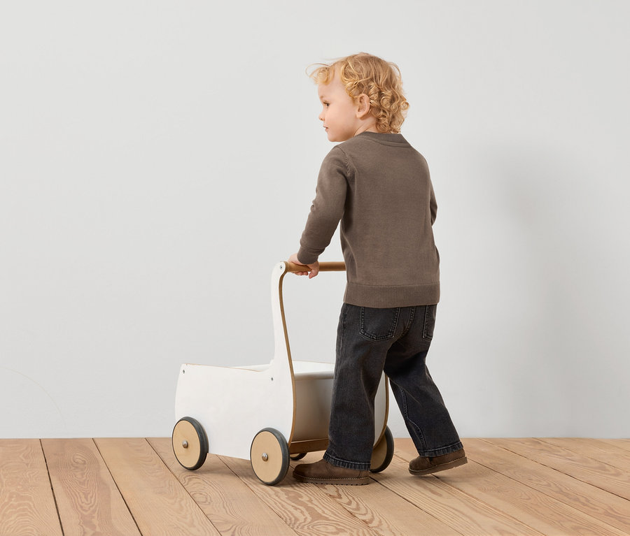 Chlapeček tlačí bílý vozík s hnědými koly po dřevěné podlaze.
