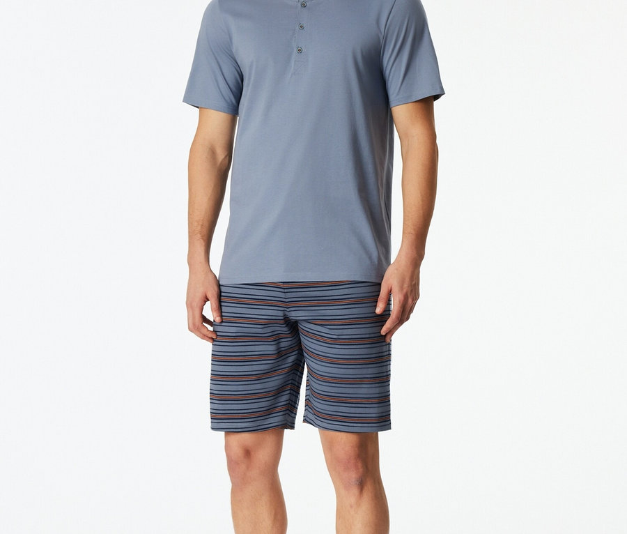 Muž v modrém pyžamovém topu s knoflíky a pruhovaných šortkách.