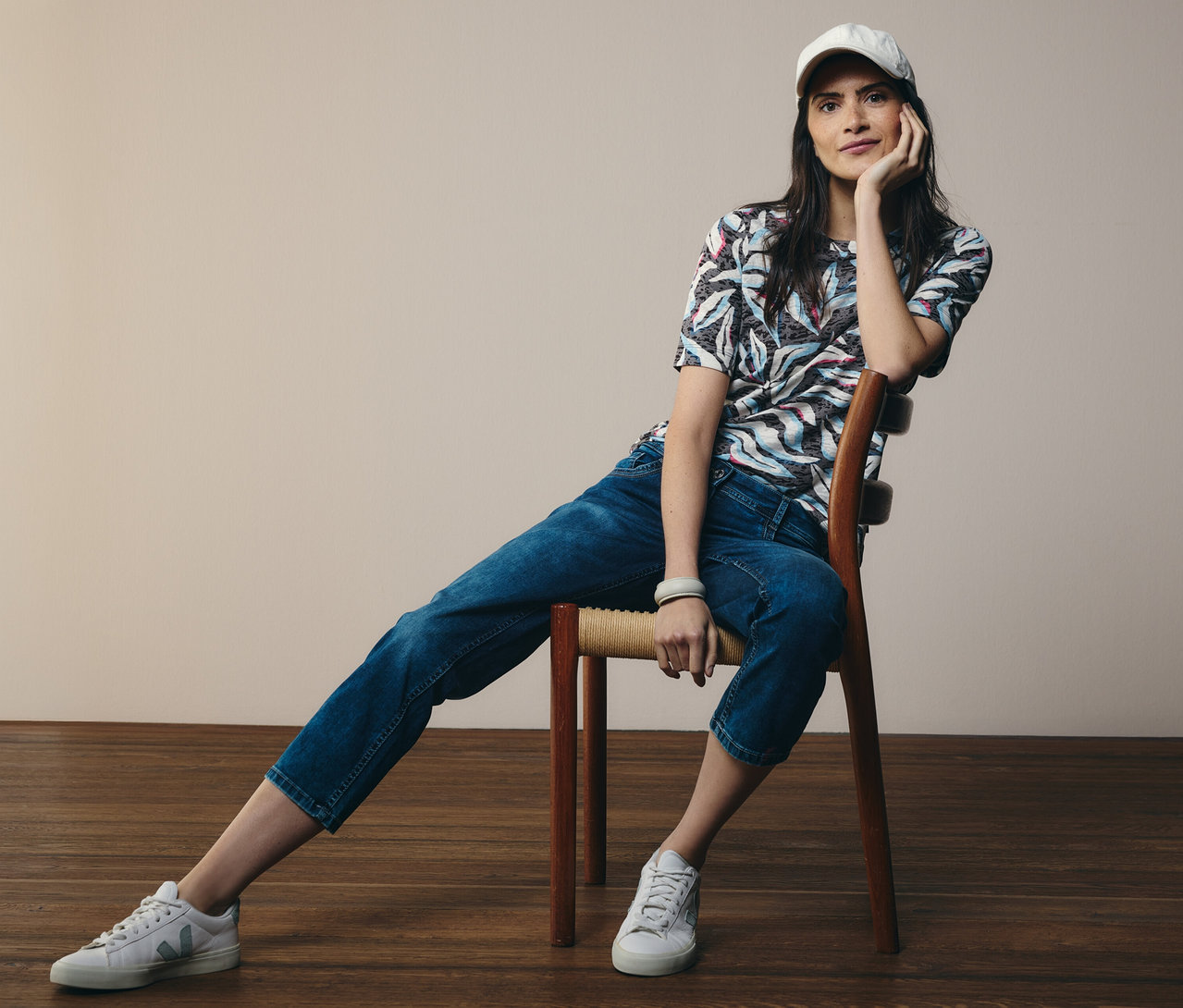 Žena sedí na židli, má na sobě modré tričko s krátkým rukávem CECIL a džíny CECIL »Scarlett«.