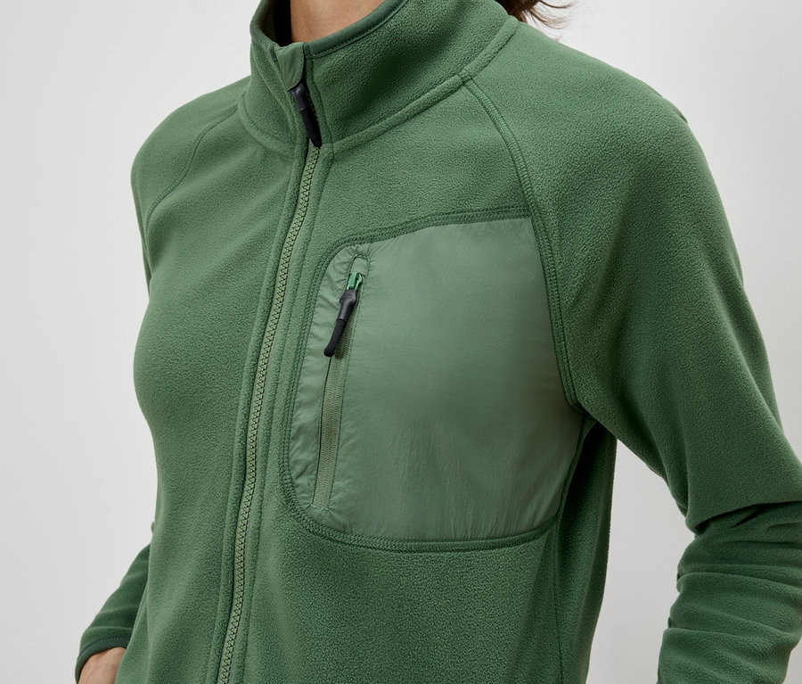 Detailní záběr ženy v zelené fleecové bundě na zip s náprsní kapsou.