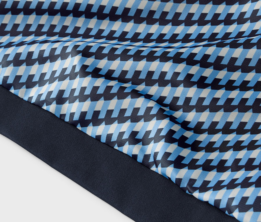 Detail látky s modrým, světle modrým a bílým geometrickým vzorem a tmavě modrým lemem.