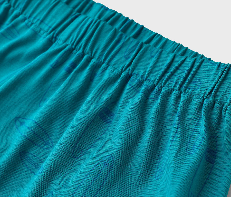 Detailní záběr tyrkysových šortek s elastickým pasem a modrým vzorem surfového prkna.