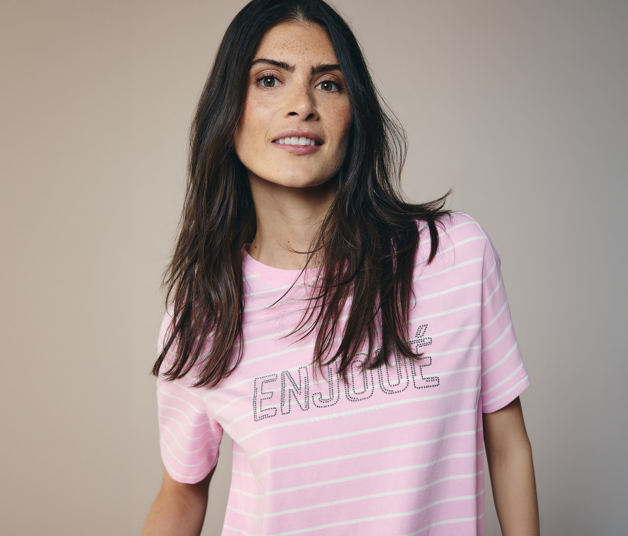 Žena s dlouhými tmavými vlasy má na sobě tričko CECIL s růžovo-bílými pruhy a nápisem 'ENJOUE'.