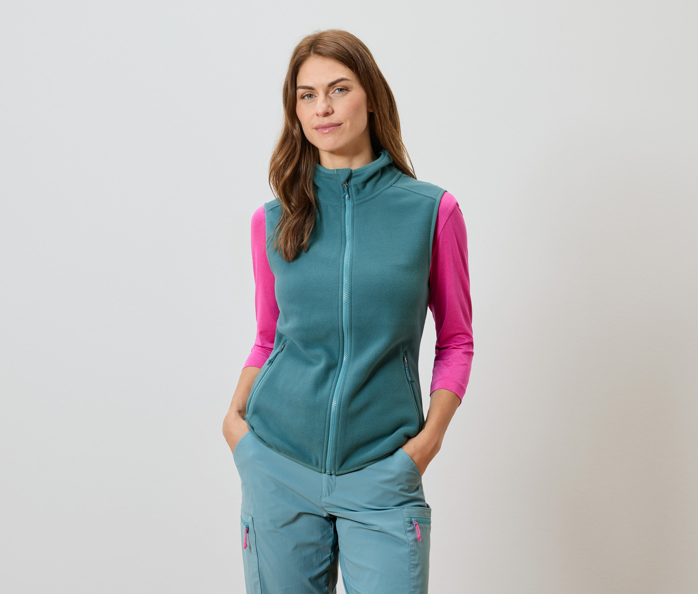 Žena v petrolejové vestě a sladěných kalhotách s růžovým trikem s dlouhým rukávem.