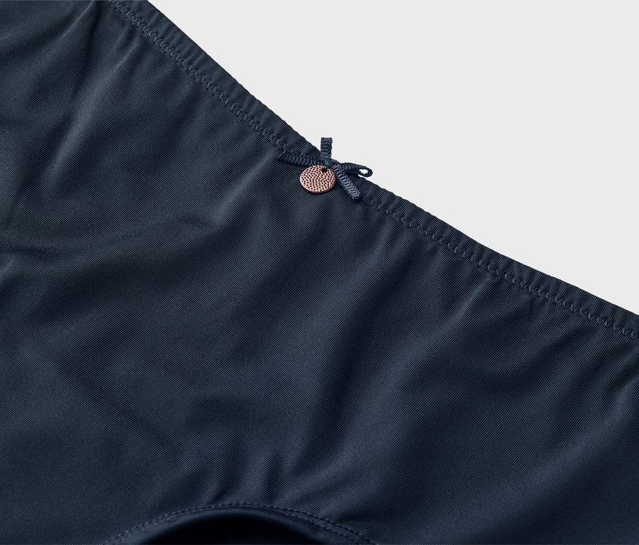 Detailní záběr na tmavě modré spodní prádlo s mašlí a malým knoflíkem.