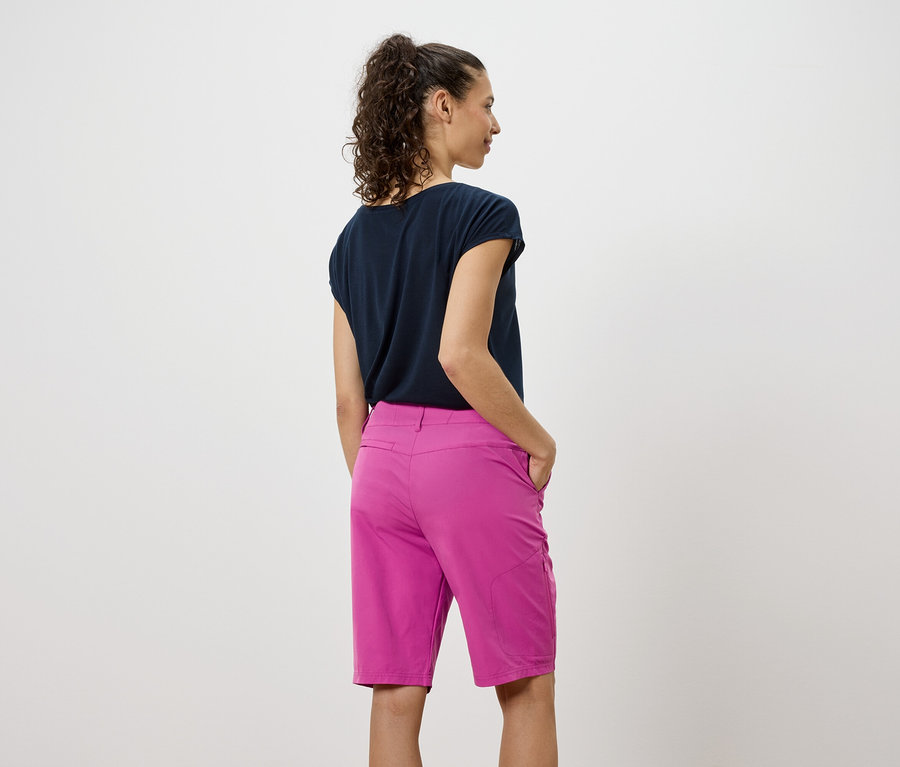 Pohled zezadu na ženu v tmavém tričku a růžových šortkách.