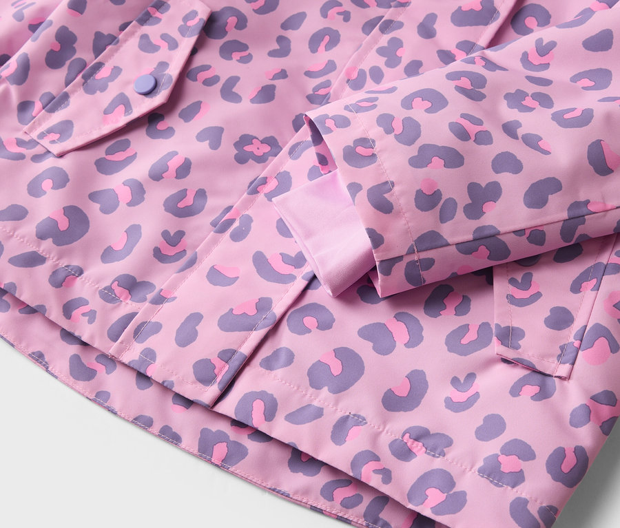 Detail růžové bundy s fialovým leopardím vzorem, knoflíkem na kapse a detaily rukávů.