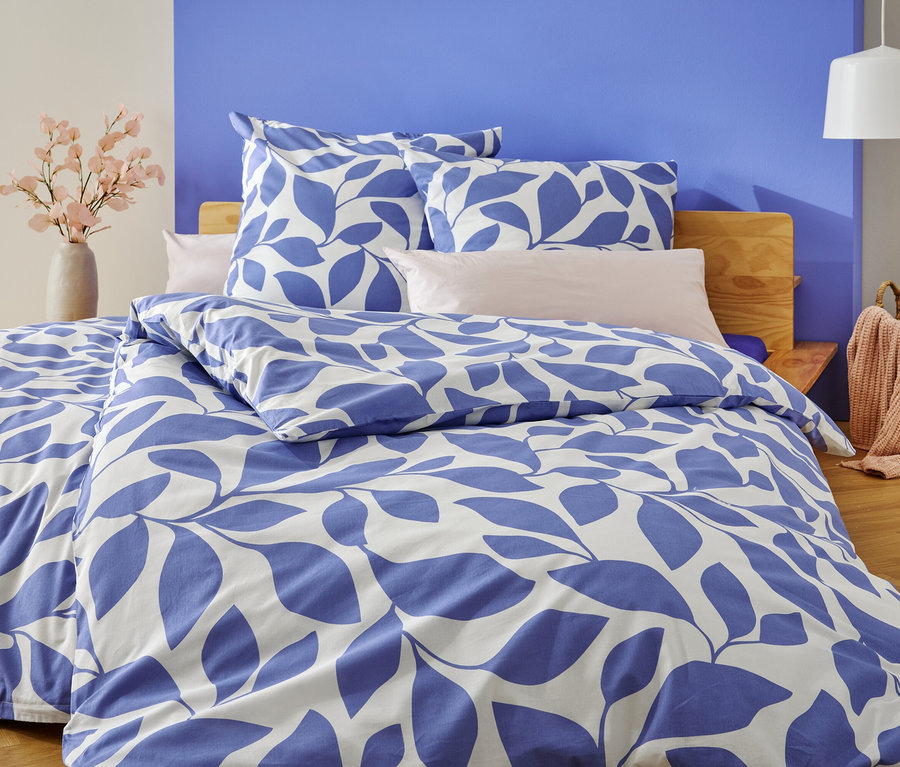 Postel s modrobílým ložním prádlem s listy stojí před modrobíle natřenou stěnou.