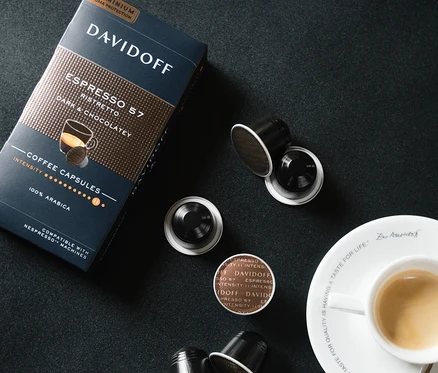 Balení a několik kapslí DAVIDOFF CAFÉ Espresso 57 Ristretto vedle šálku espressa na černém pozadí.