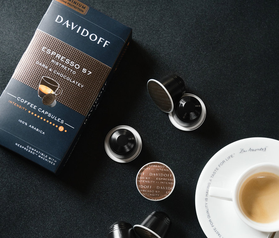 Balení a několik kapslí DAVIDOFF CAFÉ Espresso 57 Ristretto vedle šálku espressa na černém pozadí.
