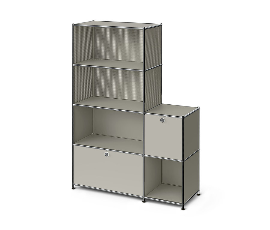 Modulární regál ve tvaru písmene L ve světle šedé barvě s chromovými rámy. Vyšší levá část má dvě otevřené police s perforovanými bočnicemi, jednu otevřenou polici s plnými bočnicemi a uzavřenou skříňku s úchytkou. Kratší pravá část má uzavřenou skříňku s úchytkou a otevřenou polici pod ní.