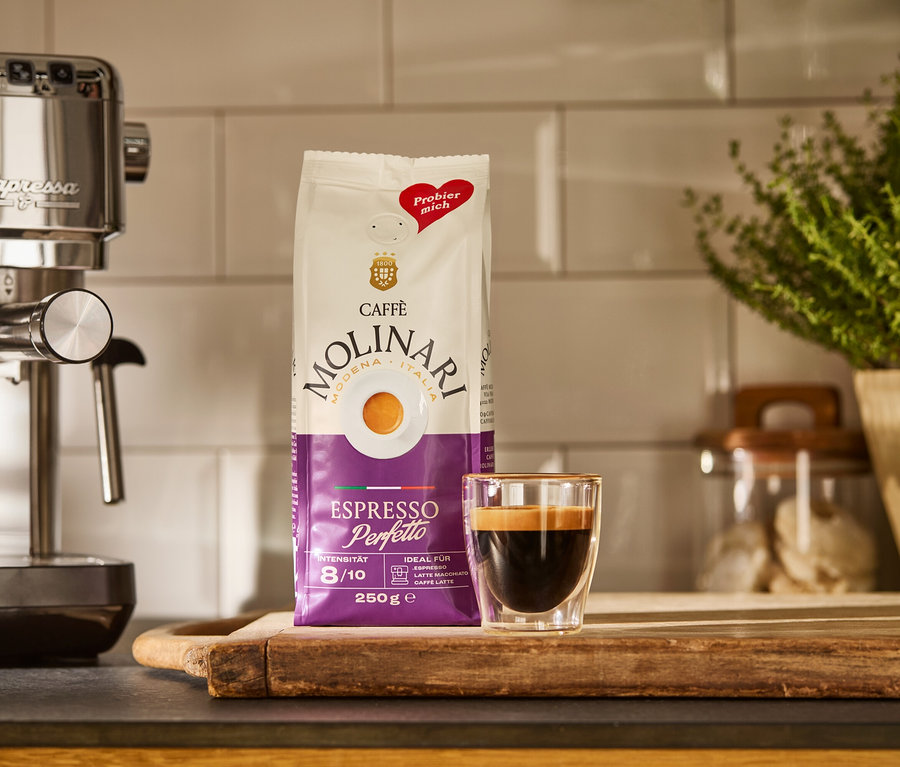Stříbrný kávovar »Lapressa«, balíček Caffè Molinari a šálek espressa na dřevěném prkénku.