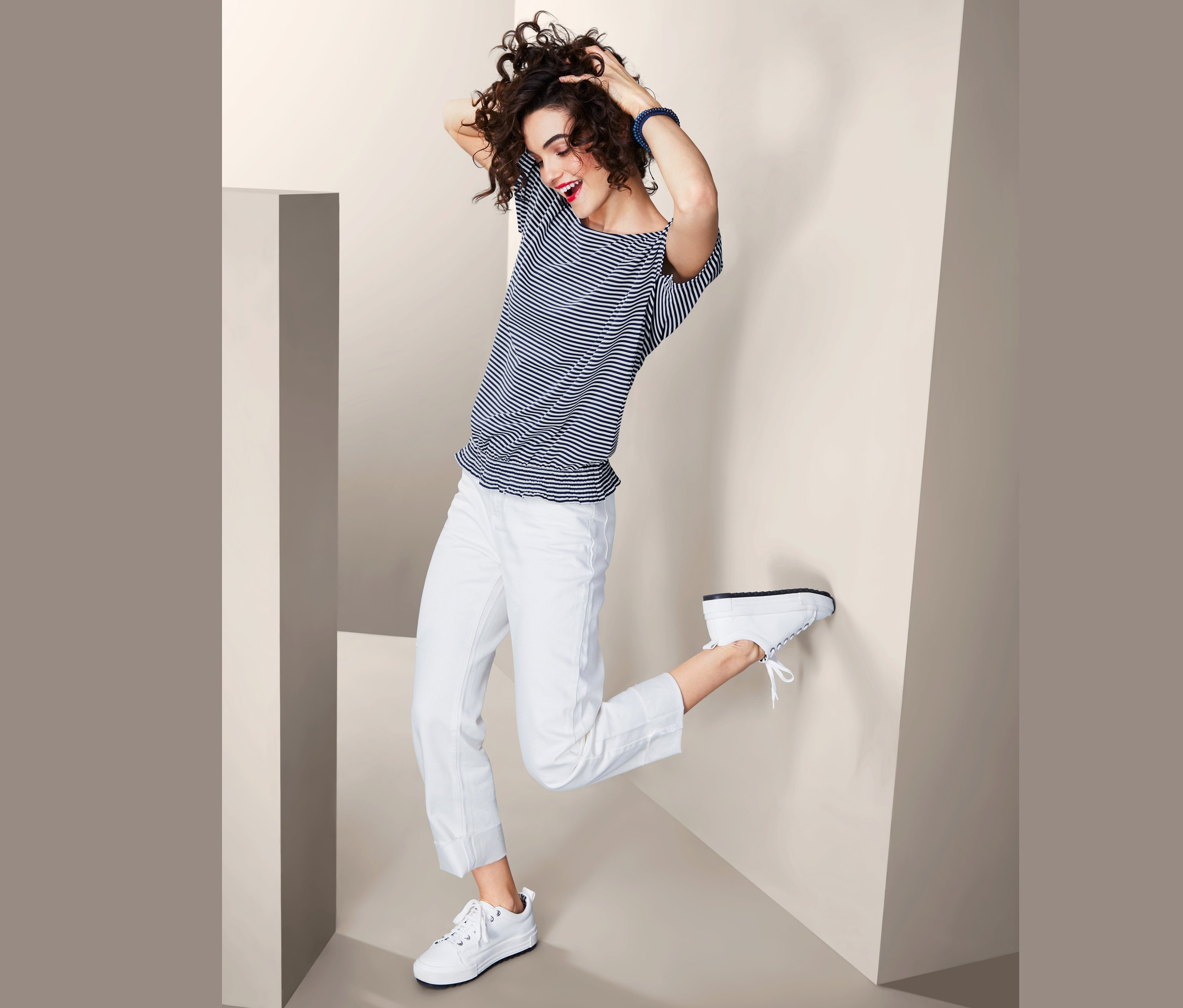 Žena pózuje v bílých kalhotech a pruhovaném triku s krátkým rukávem.