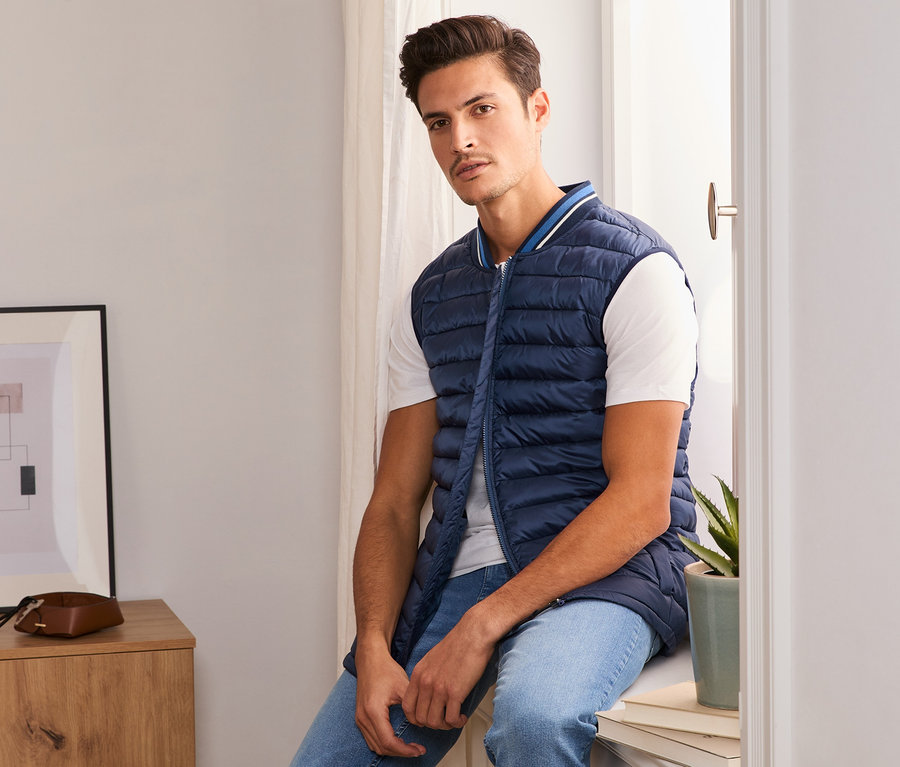 Muž sedí na parapetu v modré prošívané vestě.