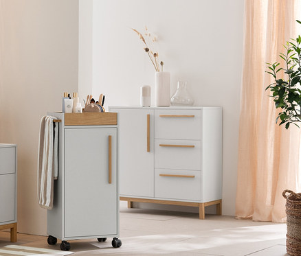 Světle šedá koupelna s vysokou skříňkou »Eklund«, skříňkou pod umyvadlo se zásuvkami a odkládací skříňkou. Dále béžovo-bílé ručníky, předložka a úložné košíky.