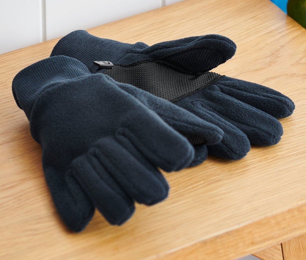 Na dřevěné lavici leží dětské fleecové rukavice vedle batohu a skateboardu.