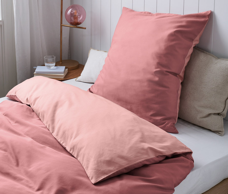 Detail pohledu na postel s růžovým bavlněným povlečením s vláknem Tencel™ různých velikostí.