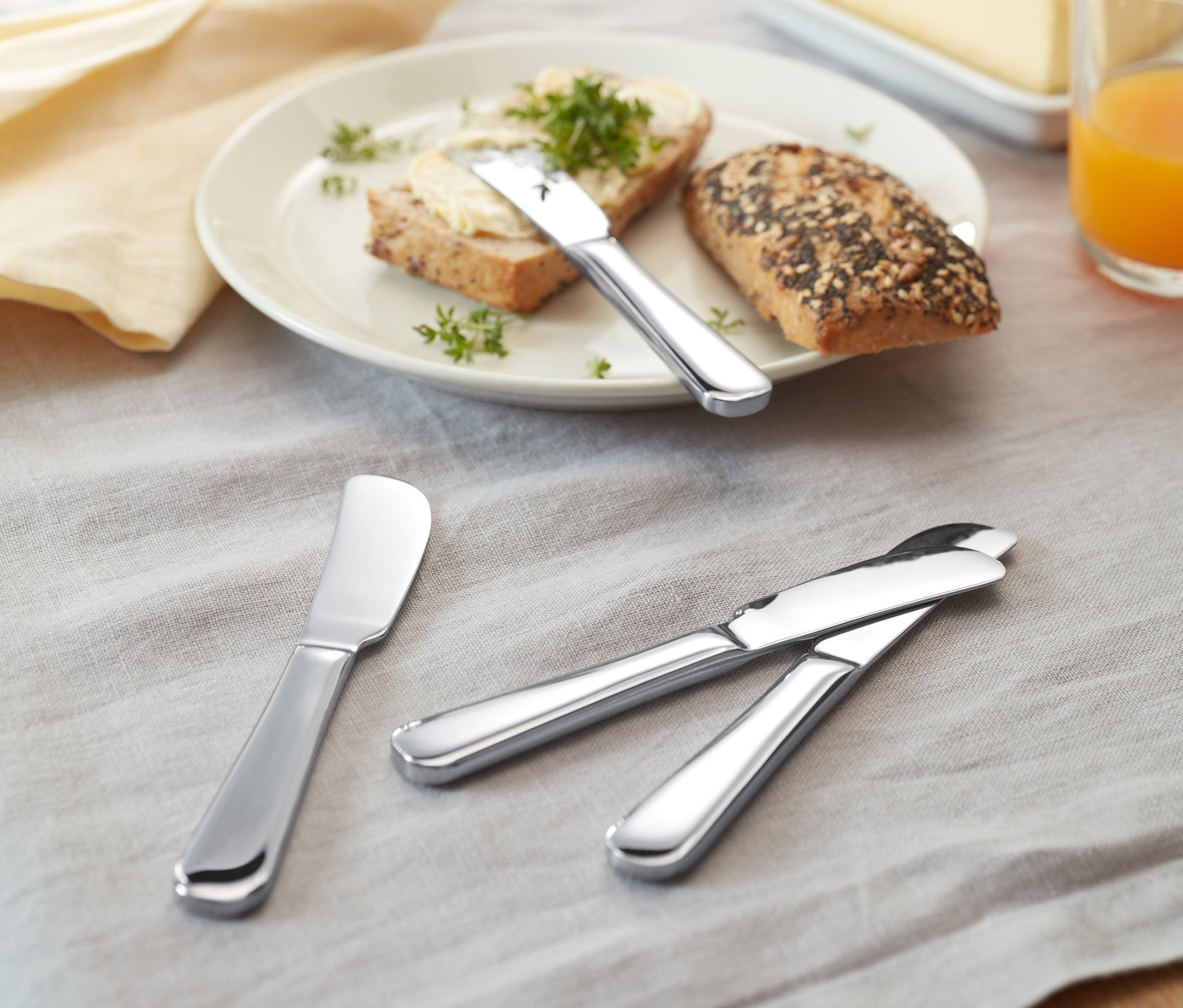 Na stole leží chleba s máslem a 4 nože na máslo.