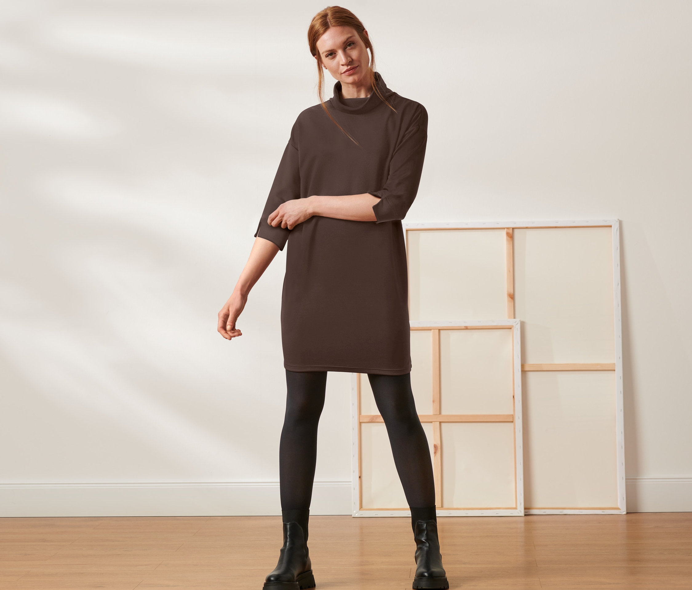 Žena pózuje v hnědých teplákových šatech.