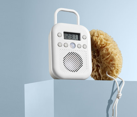 Na modrém podstavci stojí bílé rádio do koupelny a přírodní mycí houba.