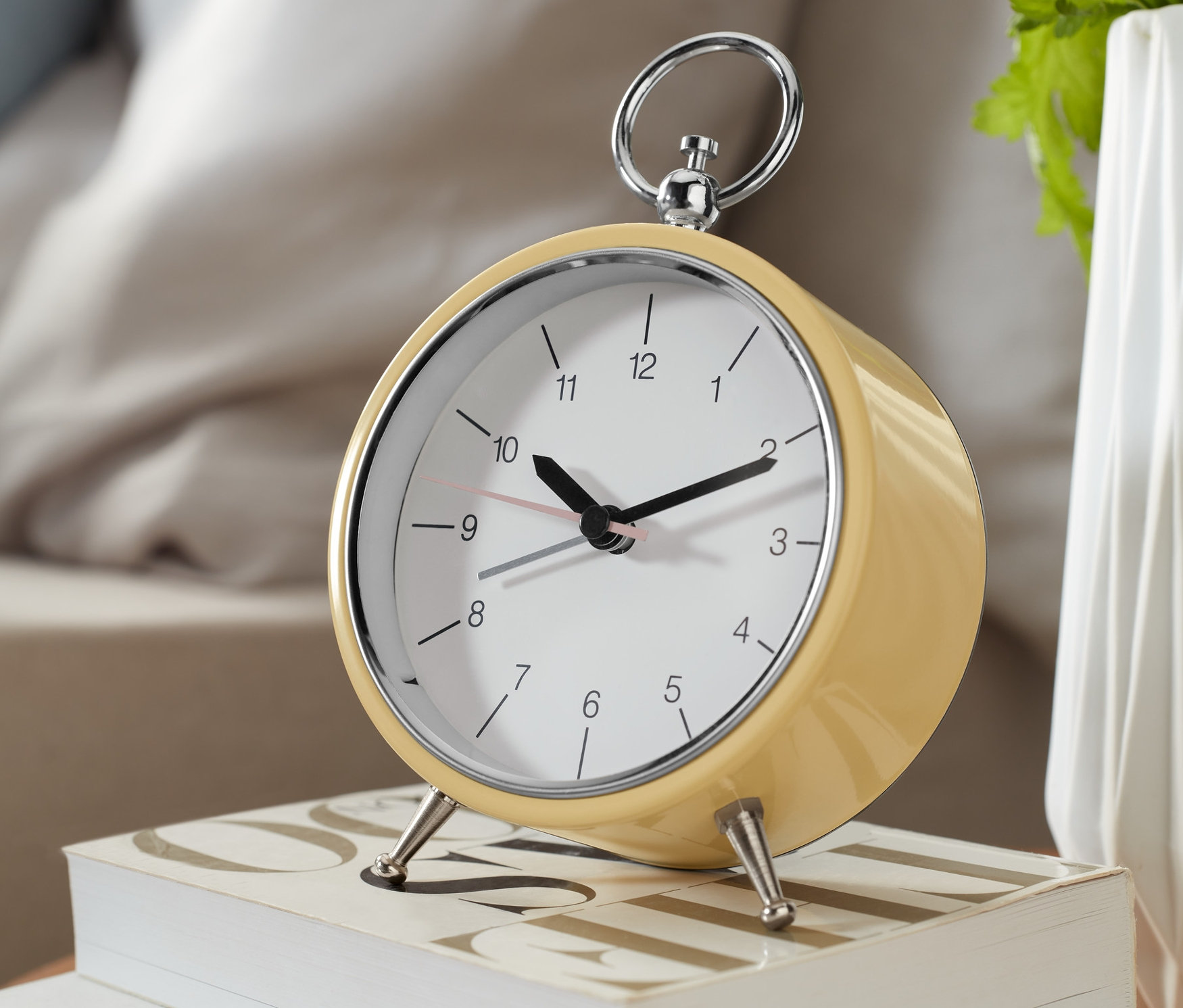 Žlutý analogový budík v retro stylu stojí na dvou bílých knihách.