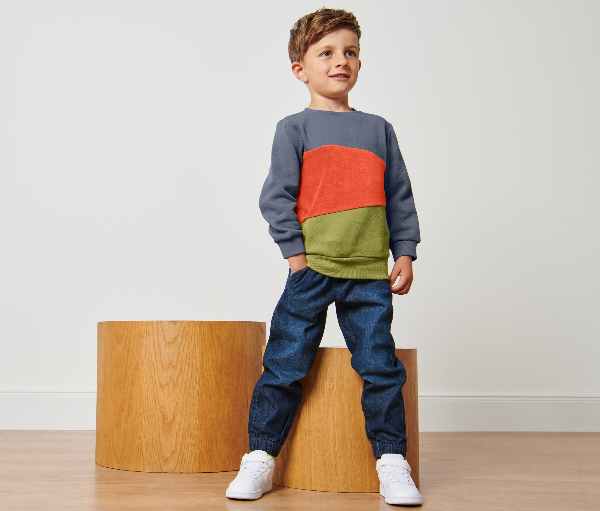 Chlapec stojí a má na sobě mikinu pro batolata a džíny.