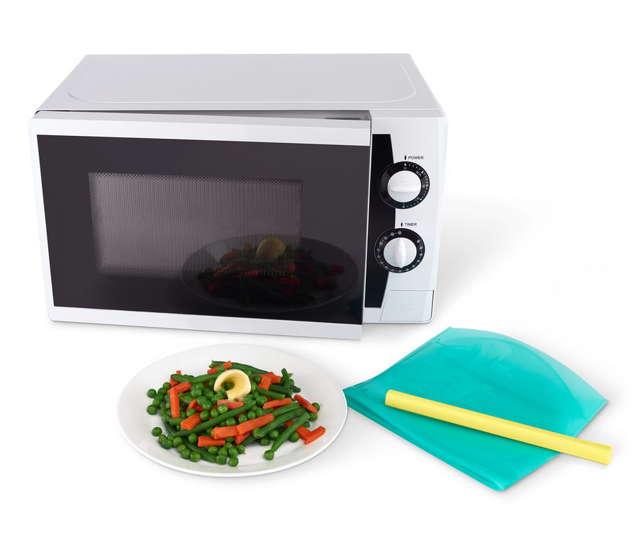 Talíř zeleniny a 2 sáčky na potraviny leží vedle otevřené mikrovlnné trouby.