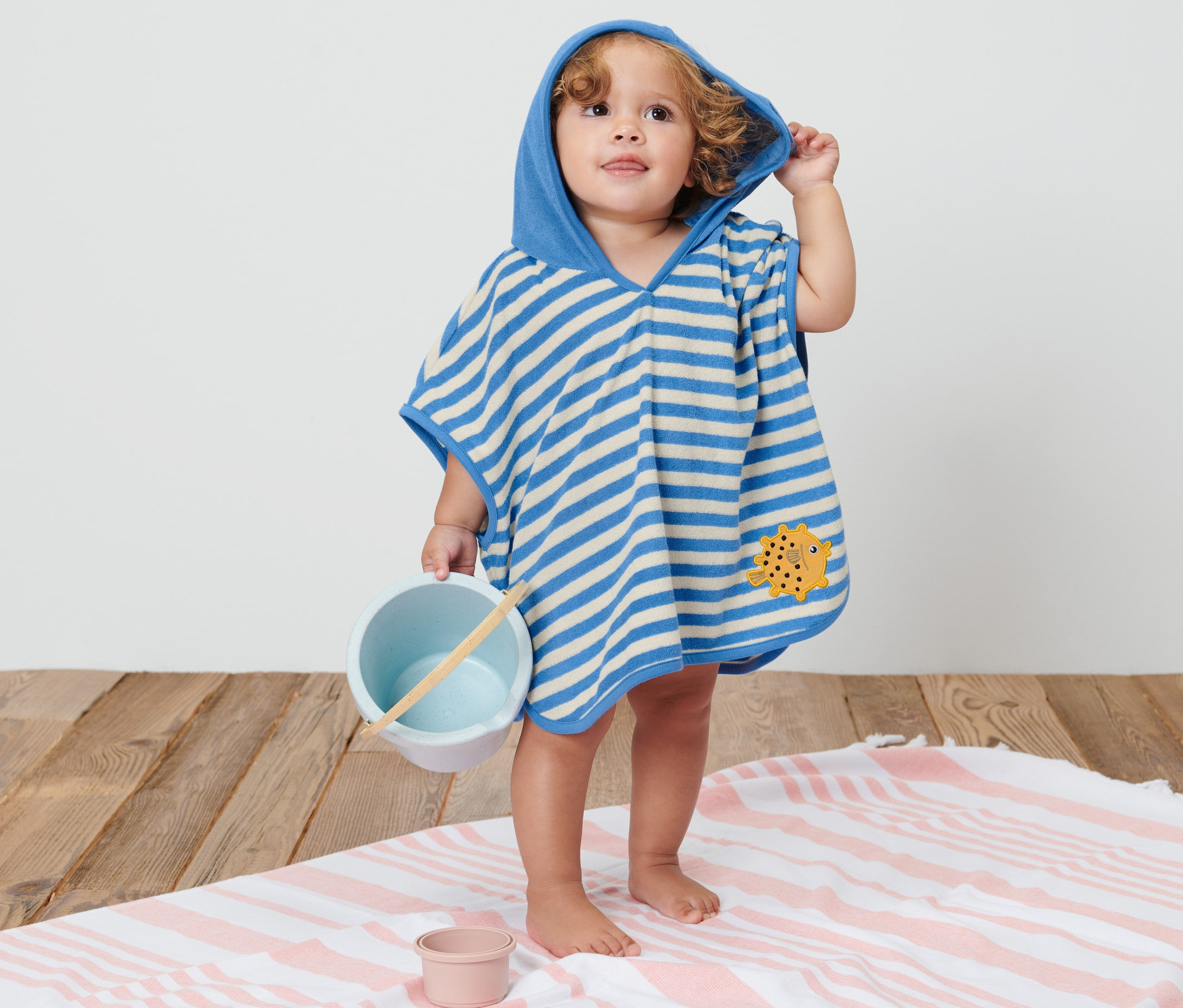 Dítě v pruhovaném ponču z froté s kapucí drží hračku.
