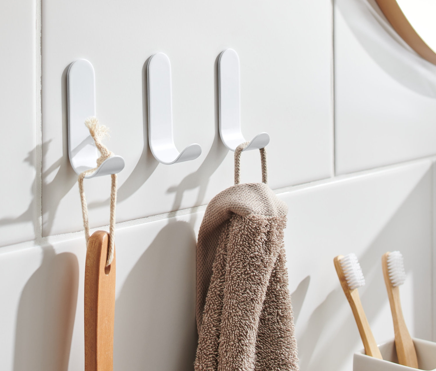 Na bílých dlaždicích visí tři samolepicí háčky, na kterých visí kartáč a ručník.