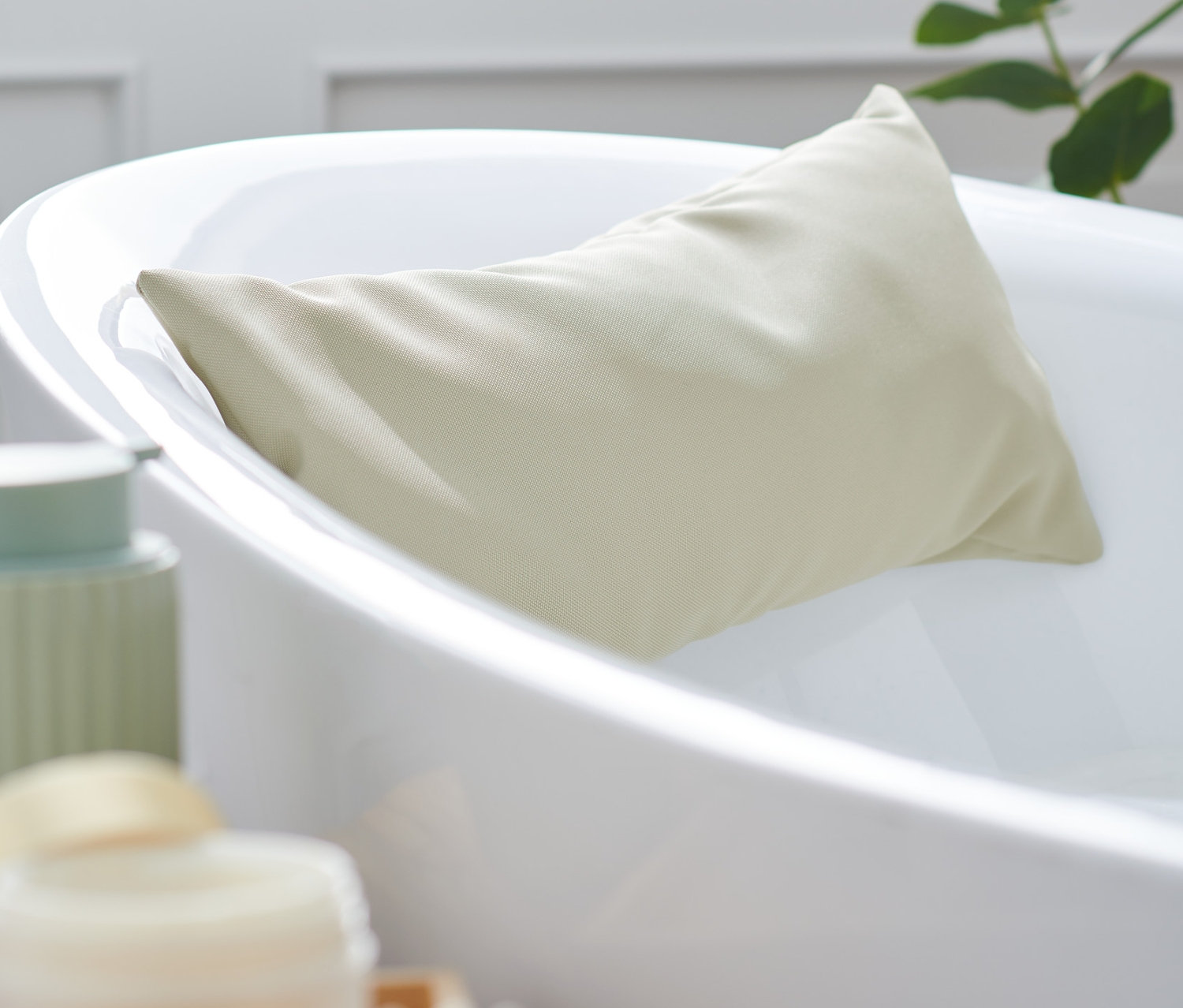 Béžový polštářek do vany je opřený o bílou vanu.