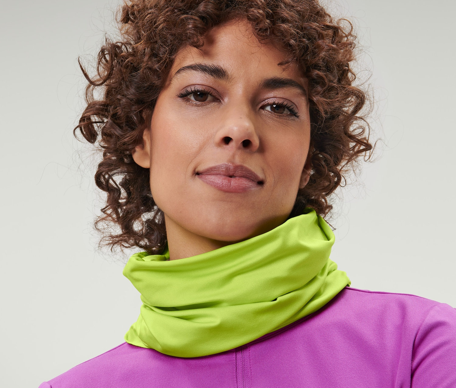 Portrét ženy s hnědými kudrnatými vlasy, která má na krku žlutý multifunkční šátek.