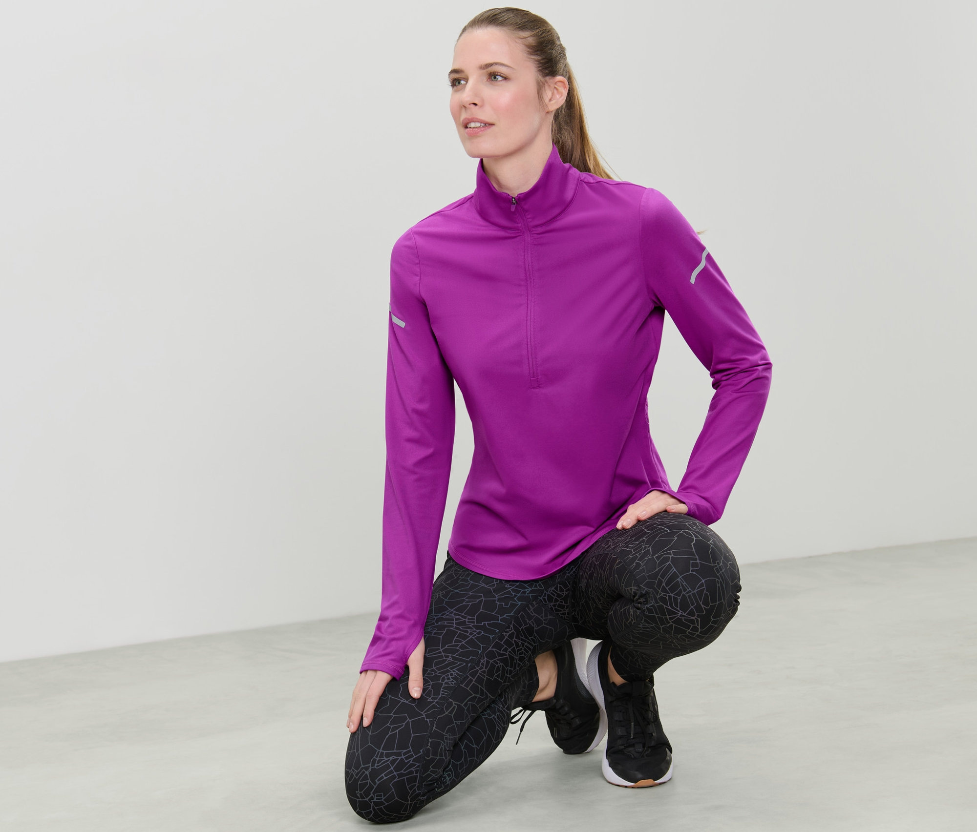 Žena v neonově bobulovém funkčním termotriku pózuje na podlaze.