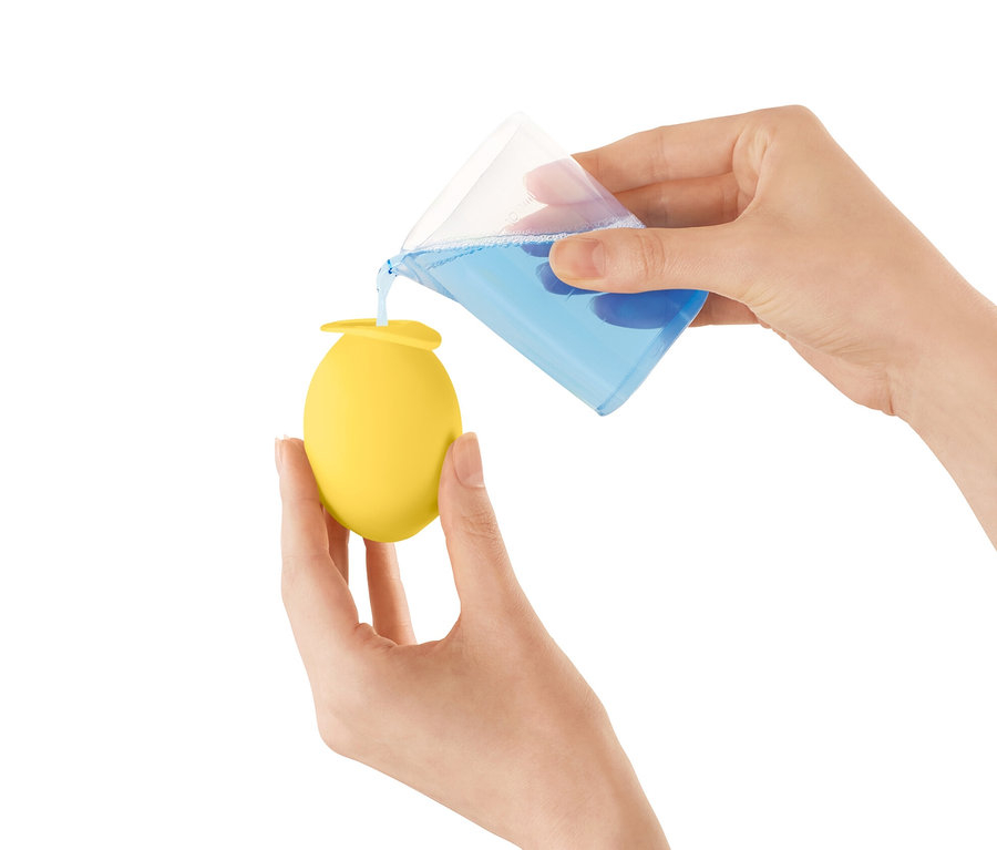 Žena nalévá modrou tekutinu z odměrky do žlutého odvápňovacího nástavce na vodovodní kohoutek.