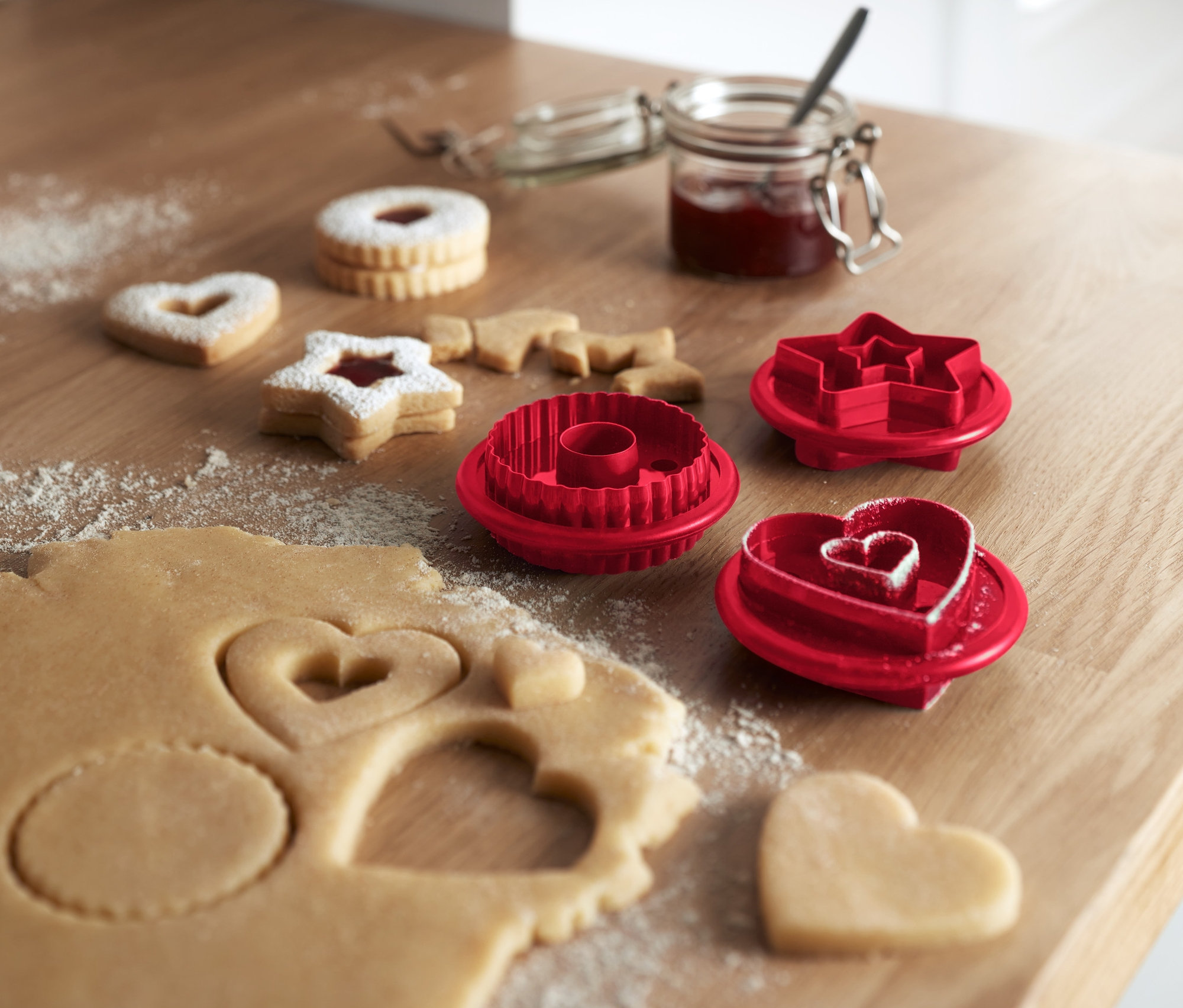 Na dřevěném stole leží linecké cukroví a vykrajovátka na linecké cukroví, 3 ks.