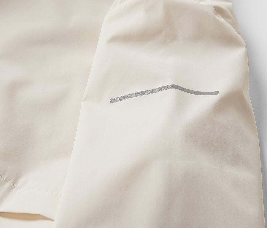 Detail krémové větruvzdorné běžecké bundy.