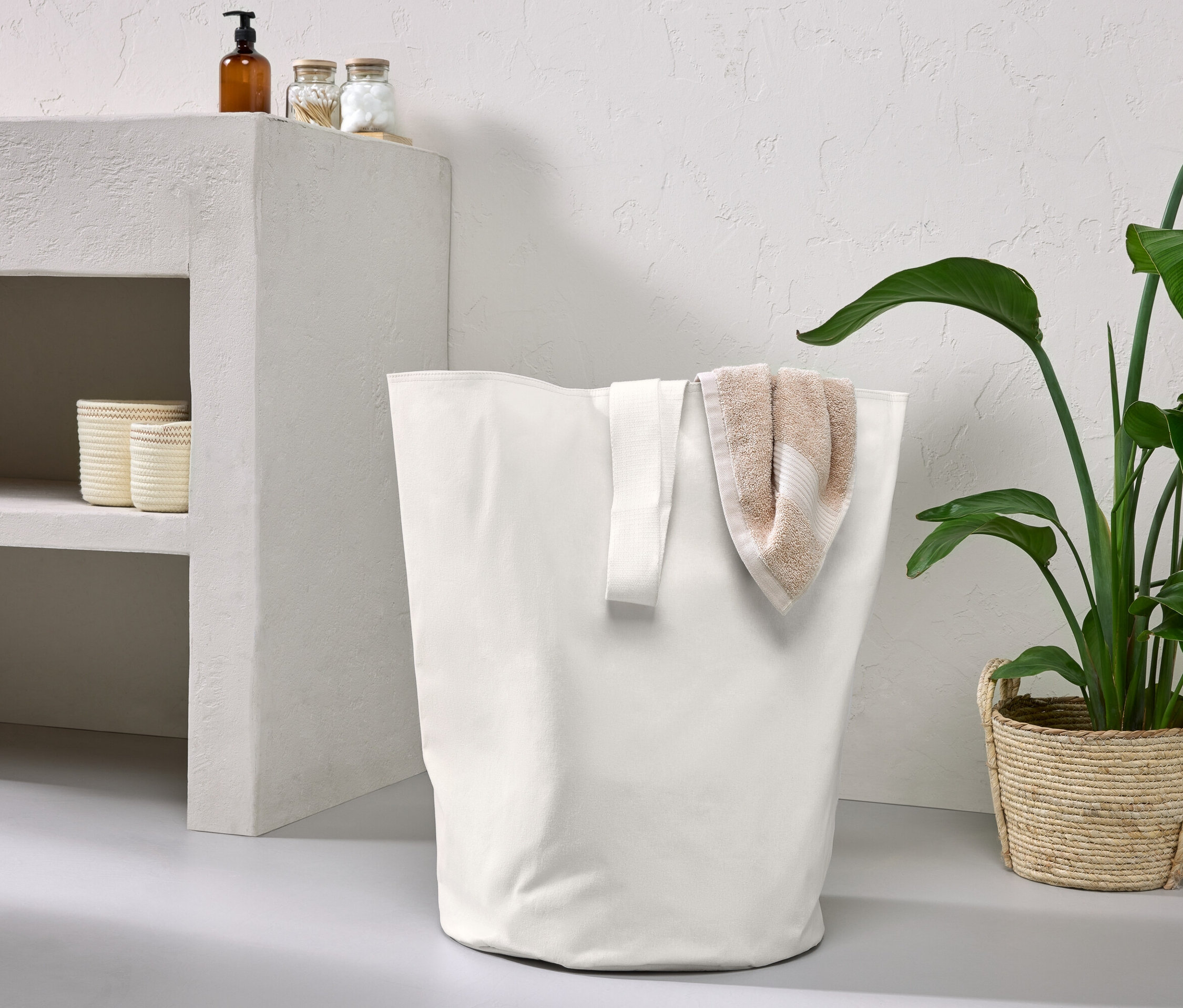 Krémový úložný koš s popruhem na přenášení a béžový ručník.