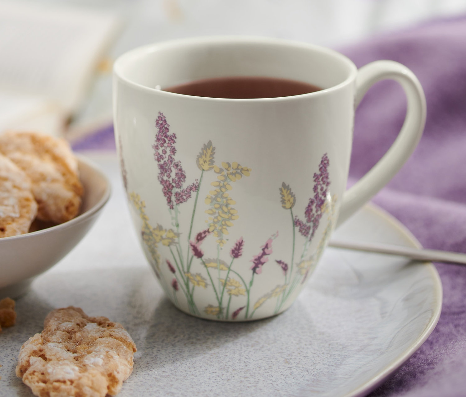 Naaranžovělé sušenky v misce a hrnek s květinovým vzorem na talíři.