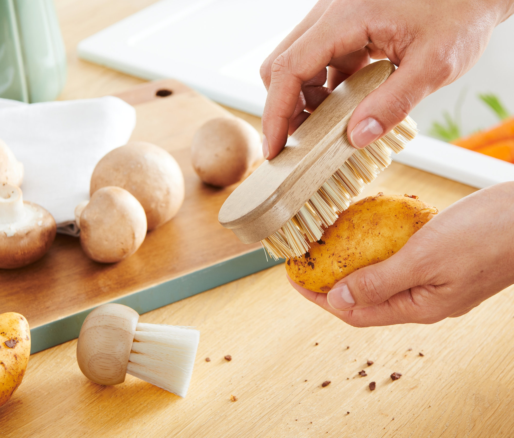 Osoba čistí bramboru pomocí 2 kartáčků na zeleninu.