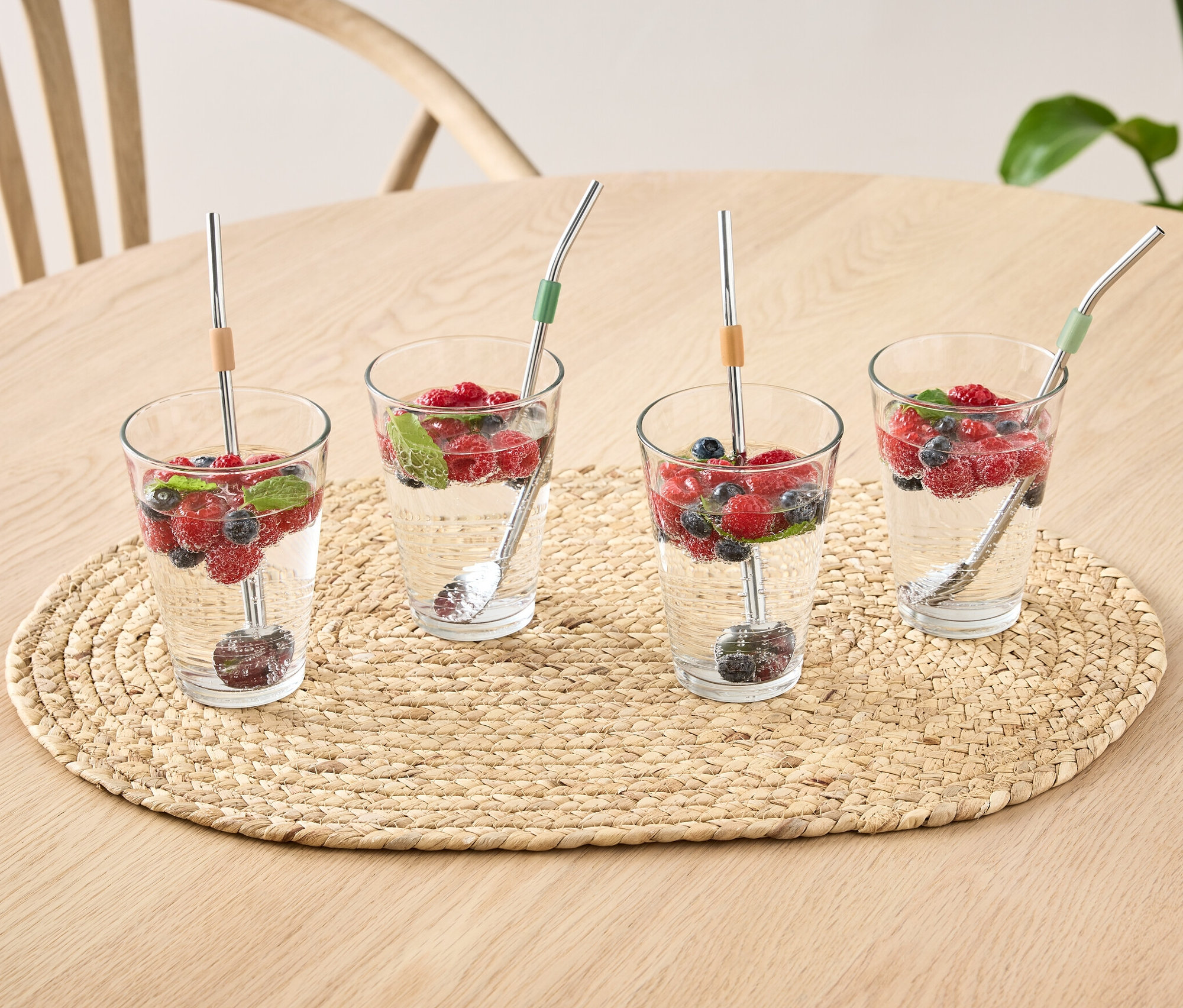 Čtyři sklenice s vodou, ovocem a lžičkami na stole.