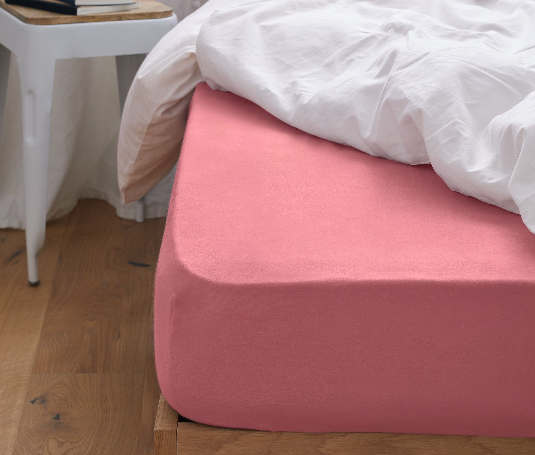 Růžové napínací prostěradlo z biberu na posteli s bílými peřinami. Vedle postele stojí stolek s vázou.