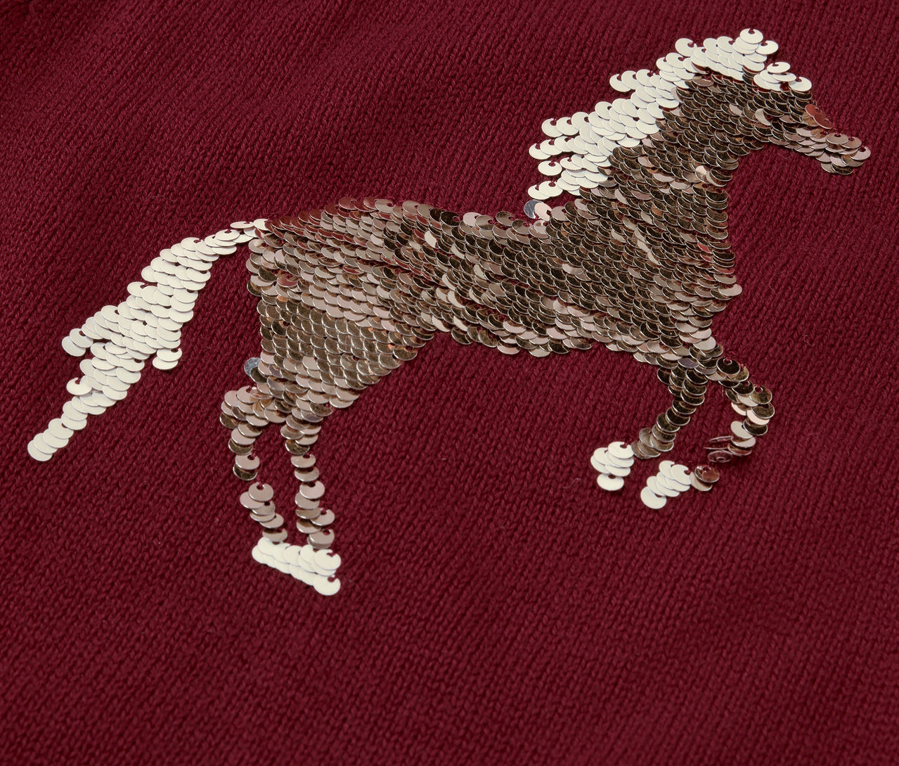 Detailní záběr na dětský pletený svetr s motivem koně zdobeným flitry.